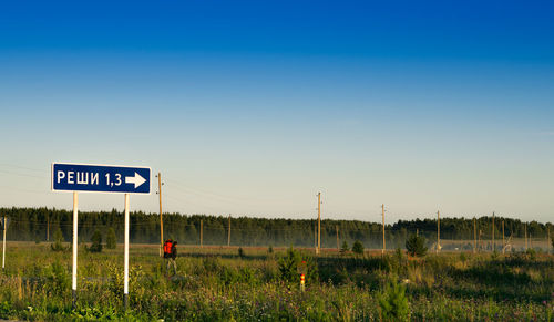 Road sign on field against clear sky