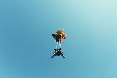 Low angle view of people paragliding against clear blue sky