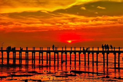 Silhouette wooden pier on sea against orange sky