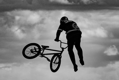 Rear view full length of man doing stunt with bicycle against sky