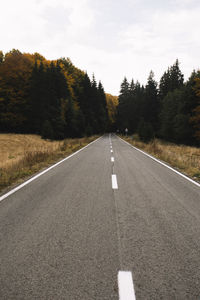 Empty road amidst trees against sky