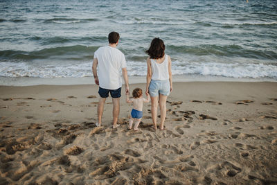 Husband and wife with son looking at view while standing on beach during sunset