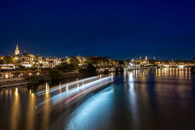 Illuminated buildings by river against sky at night