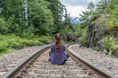 Rear view of woman sitting on railroad track