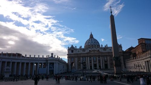 Tourists in front of building against cloudy sky