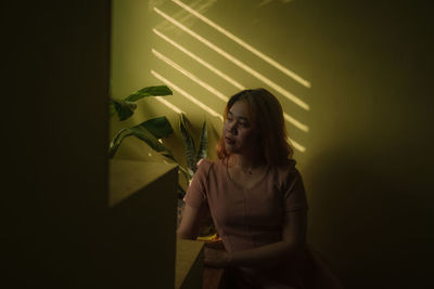 Woman looking away while standing against wall at home