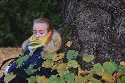 Portrait of young woman by tree trunk