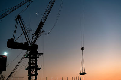 Low angle view of silhouette cranes against sky during sunset