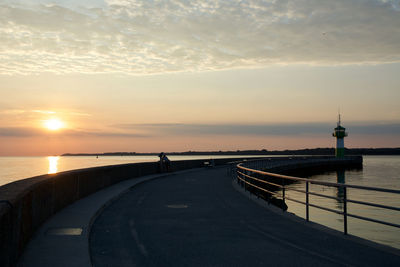 Road by sea against sky during sunset