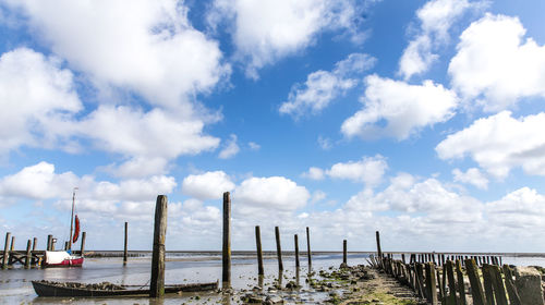 Wooden posts at beach against cloudy sky