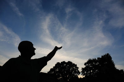 Optical illusion of silhouette man touching clouds