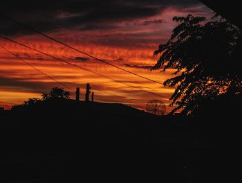 Silhouette trees on landscape against orange sky