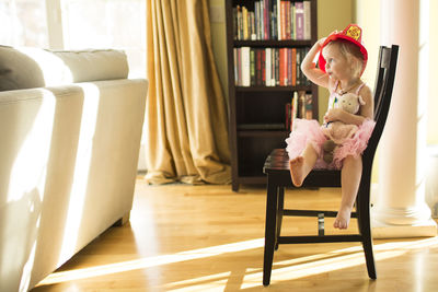 Little blonde girl wearing fire hat and tutu, holding a baby doll