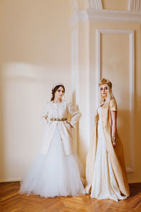 Portrait of young women in dress standing against wall