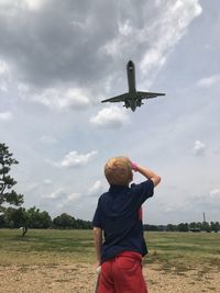 Full length of airplane flying over field against sky