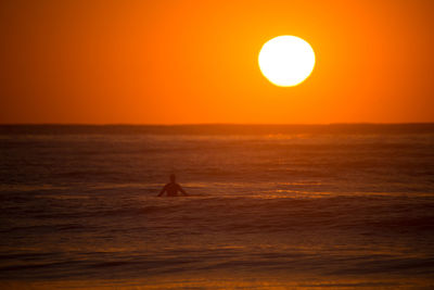 Silhouette surfer surfing in sea against sky during sunset