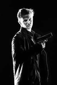 Portrait of young man holding gun against black background
