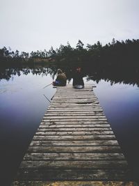 Rear view of people on jetty by lake against clear sky