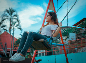 Side view of young woman sitting on swing at playground