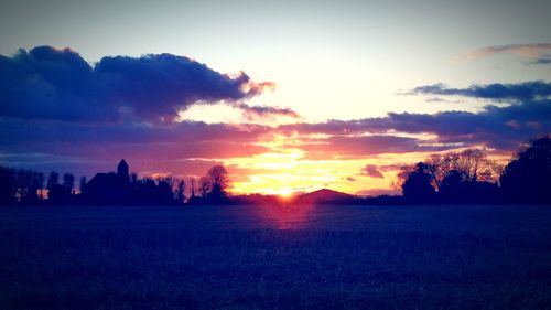 Silhouette of trees on field against cloudy sky