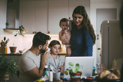 Father checking son's ear while mother standing by in kitchen