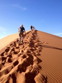 Rear view of people walking on sand at desert against blue sky