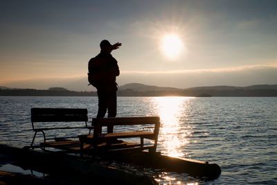 Hiker silhouette with backpack on abandoned pedal boat in the sunset. autumn sunny day at sea