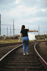 Rear view of woman on railroad tracks against sky