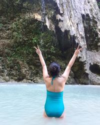 Rear view of woman with arms raised in sea against rock formation