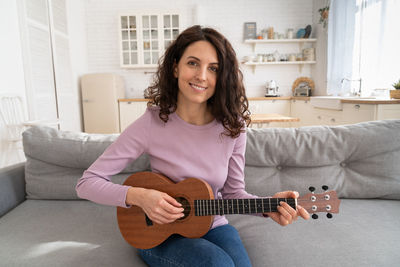 Portrait of smiling woman playing ukulele at home