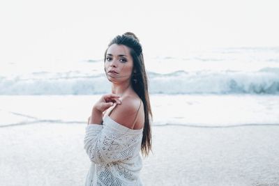 Portrait of beautiful young woman standing at beach against sky