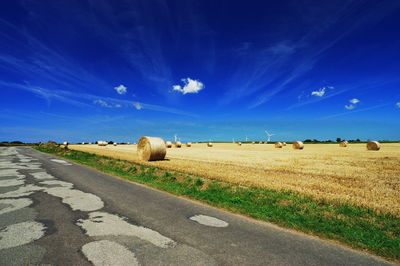 Road by agricultural field against blue sky