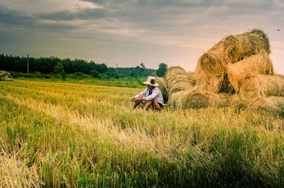 Man sitting on field against sky