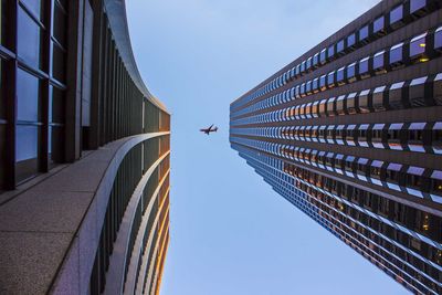 Directly below shot of airplane flying over modern buildings against clear sky