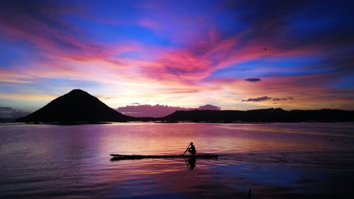 Silhouette man in sea against sky during sunset