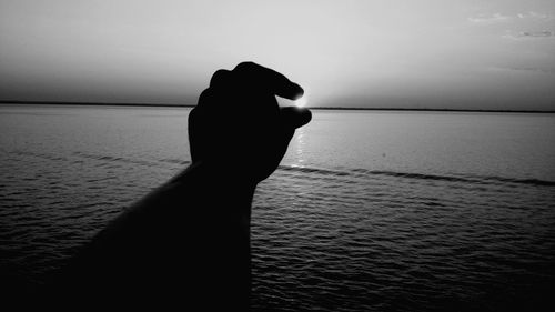 Close-up of silhouette hand against sea