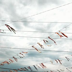 Low angle view of ribbons hanging on cables against sky