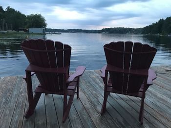 Empty chairs and table by lake against sky