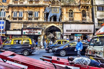 People on street by cars against old building in city