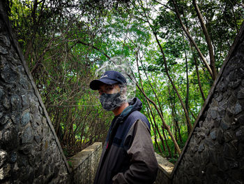 Side view of man standing by tree trunk in forest