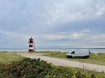 Lighthouse by sea against sky with campervan