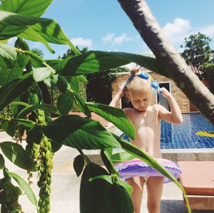 Girl standing by plant at poolside on sunny day