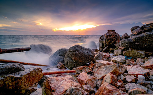 Ocean water splash on rock beach with beautiful sunset sky and clouds. sea wave splashing on stone