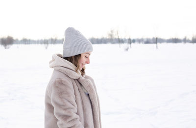 Young girl in beige clothes, fur coat made of artificial fur walks in winter