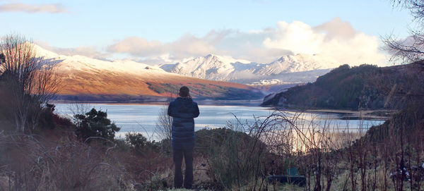 Rear view of man standing by lake against sky