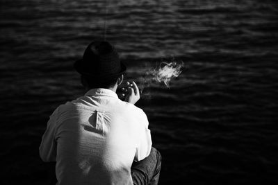 Rear view of man smoking while sitting by sea