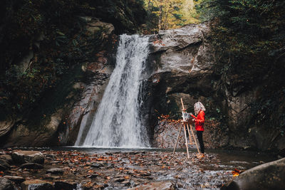 Woman painter artist painting a picture close to a waterfall