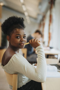 Portrait of smiling female student holding pen studying in library
