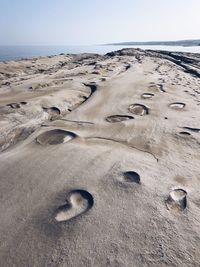 Footprints on sand at beach against clear sky