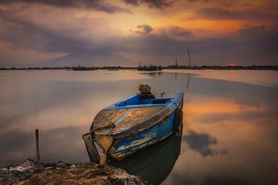 Boat moored on sea against sky during sunset